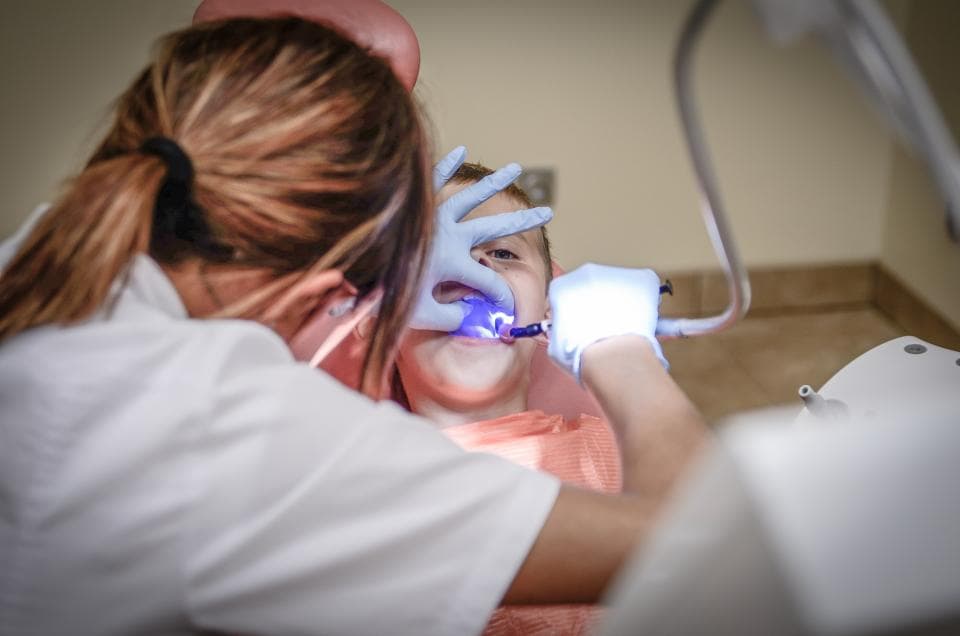 A dentist cleaning a patient's teeth under a lamp